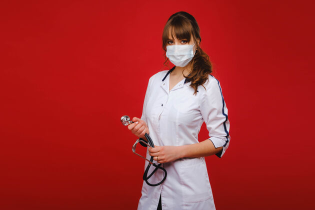 女孩一位身穿白大褂 戴着医用口罩的年轻医生站在红色的背景上药品年轻人防护