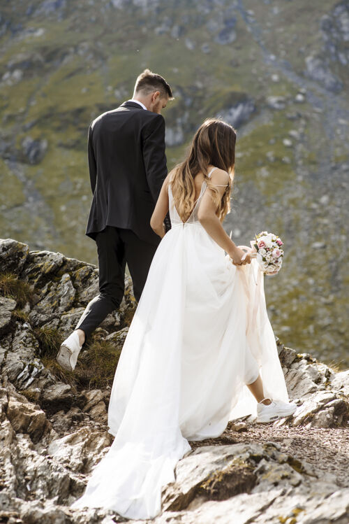 西装一只手拿着水桶 另一只手牵着新郎 在山里行走的不可辨认的新娘婚礼人庆典