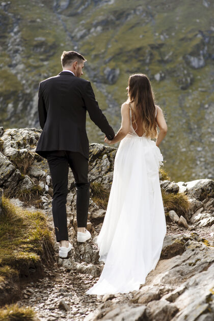 浪漫一对年轻的新婚夫妇手牵手走过大山的全景和后视图浪漫世界情侣