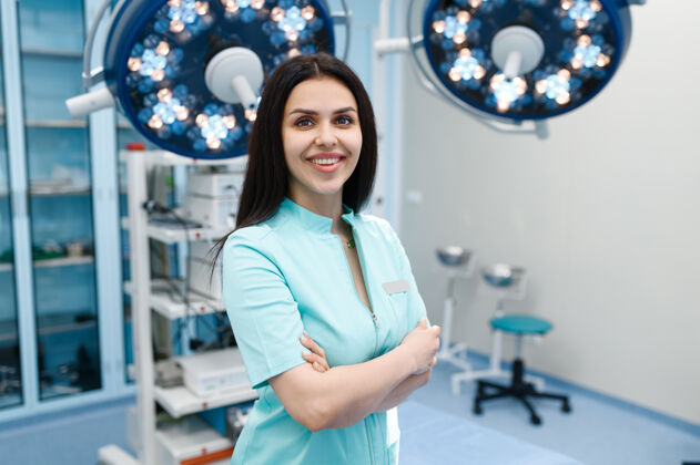 急诊室手术室里微笑的女外科医生 背景是台灯和手术台桌子药品医疗