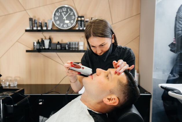 客户一个专业的发型师在一个现代时尚的理发店剃须和削减一个年轻人的头发泡沫胡子风格