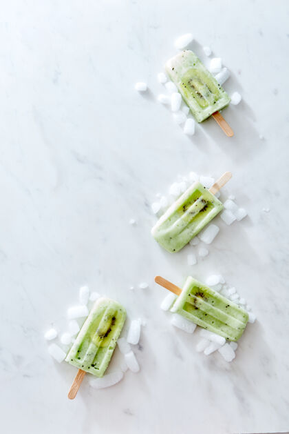 棒棒糖汽水绿色的冰激凌放在一根棍子上 上面放着一片新鲜的猕猴桃和冰 在灰色大理石背景上以角落框架的形式呈现 上面有一份空间布局为了你的想法平淡躺下果味酸橙营养