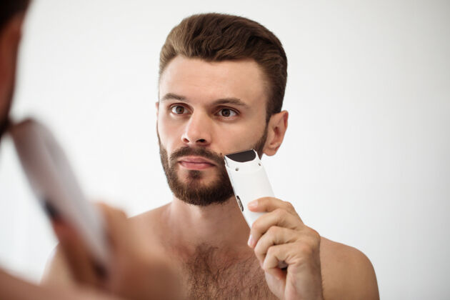 发型英俊的年轻人在街上刮胡子浴室.肖像一个时髦的裸体胡须男人在家里的镜子里检查他的脸理发师镜子男人