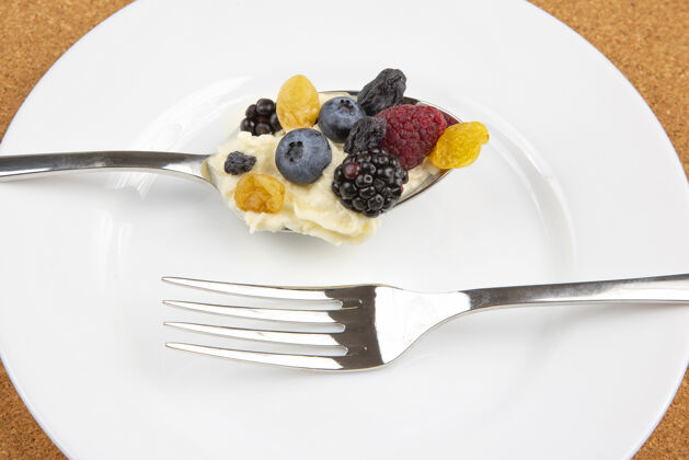 草莓覆盆子 葡萄干 黑莓 蓝莓加奶油放在勺子里放在白色的蛋糕上盘子维生素还有营养饮食浆果蓝莓