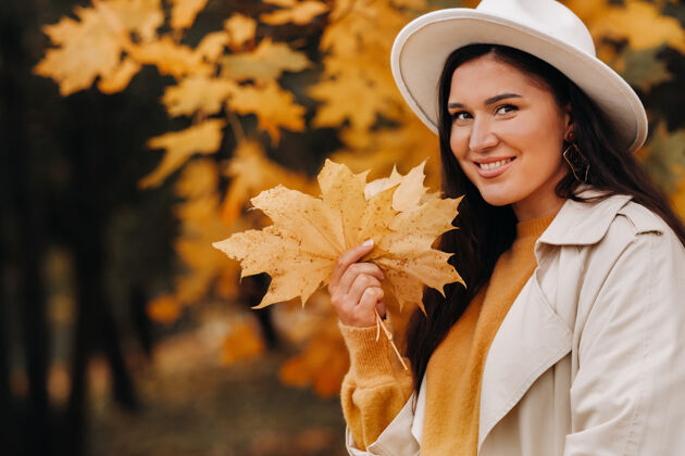 关系一个穿着白大衣戴着白帽子的女孩在秋天微笑公园肖像金秋时节的女人乐趣一起季节
