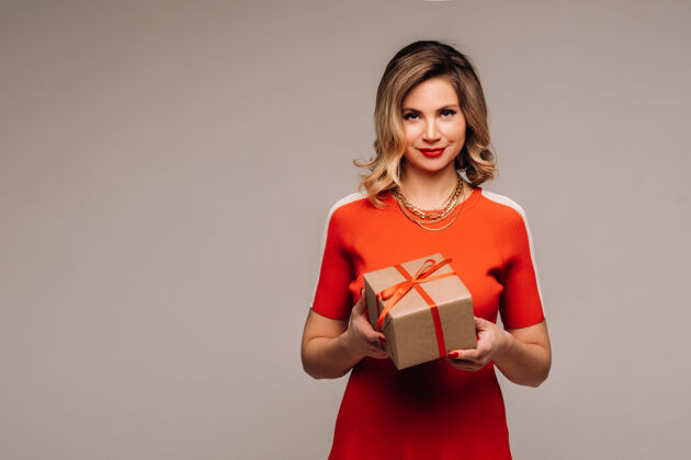 模特一个穿着红裙子的女孩手拿礼物站在灰色的墙上女孩盒子礼物