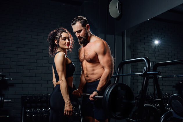 健身房黑漆漆的健身房里 一个赤膊上阵 留着胡子的家伙站在漂亮女士旁边 用沉重的杠铃练习男人努力活动