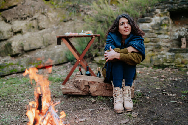 户外冬日野餐时坐在火炉旁的年轻女子快乐休闲温暖