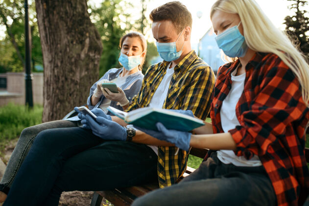 保健戴着面具的年轻人坐在公园的长椅上 隔离感染年轻人冠状病毒