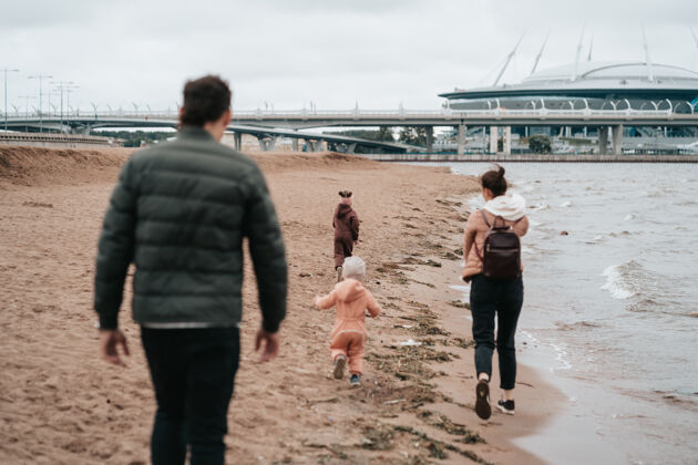 快乐幸福的一家人走在河边肖尔爸爸 妈妈和两个孩子正沿着海湾散步人团聚海滩