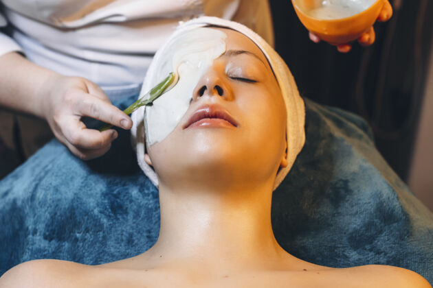 痤疮可爱的女人在健康spa中心做海藻酸钠面膜治疗美容师自然