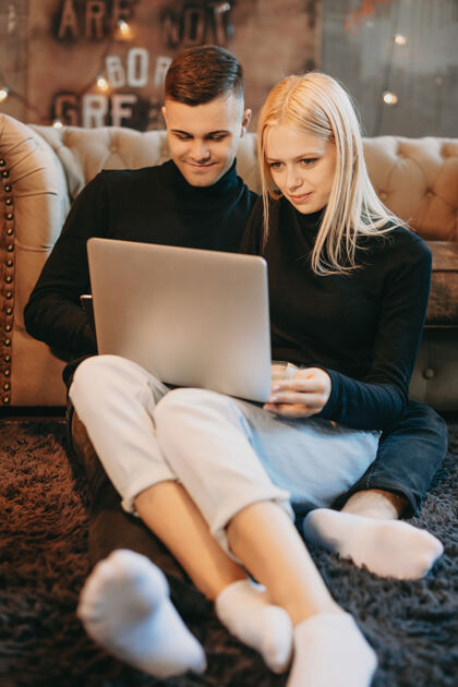 笔记本电脑一对身着黑色衣服的迷人年轻夫妇坐在地板上 看着笔记本电脑屏幕的画像平板电脑数码帅哥
