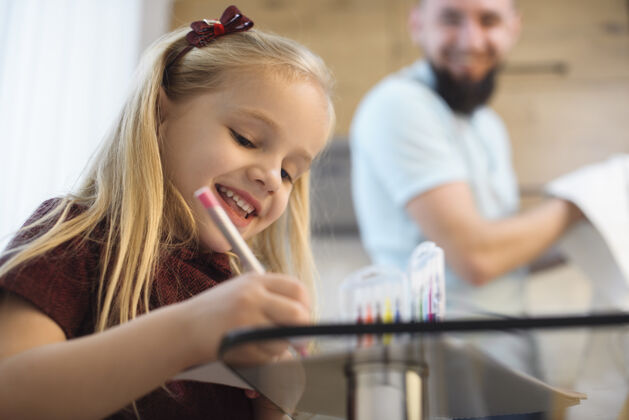 父亲快乐的金发小女孩微笑着在厨房里画画 而她的父亲正在洗碗年轻童年室内