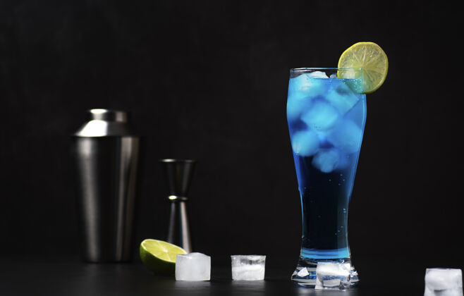 冰块一杯冰蓝色的鸡尾酒放在一个用石灰装饰的高玻璃杯里 放在深灰色的桌子上烹饪过程摇壶酸橙片