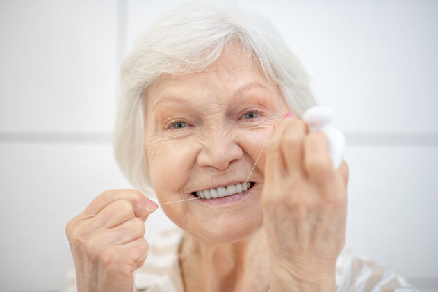 清洁打扫牙齿灰色-一个头发浓密的女人在用牙线刷牙头发花白家庭仪表堂堂
