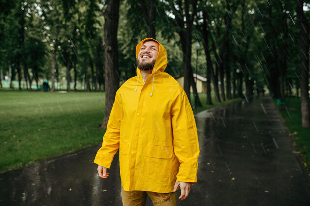 白天穿着雨衣的人在夏天享受雨水公园快乐男人穿着雨衣走在小路上 小巷里天气潮湿雨气候树枝