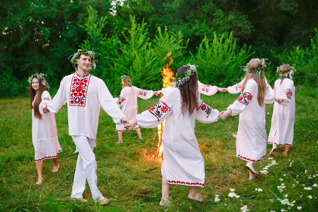 年轻仲夏年轻穿着斯拉夫人衣服的人在盛夏围着火转植物老信徒神圣