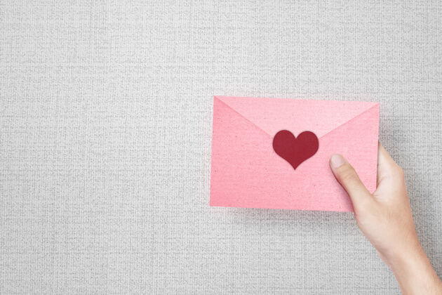 信封人手拿着一个粉红色的信封 心形有纹理的墙壁快乐礼物情人节