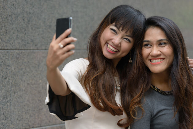 泰国两位年轻的亚洲女商人在城市户外的合影商务女性使用手机