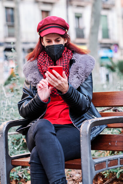 城市一名妇女戴着口罩 坐在户外使用手机公园新的正常寿命城市概念概念无线防护健康