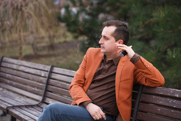 人一个年轻人坐在长凳上抽电子烟吸烟蓬松液体
