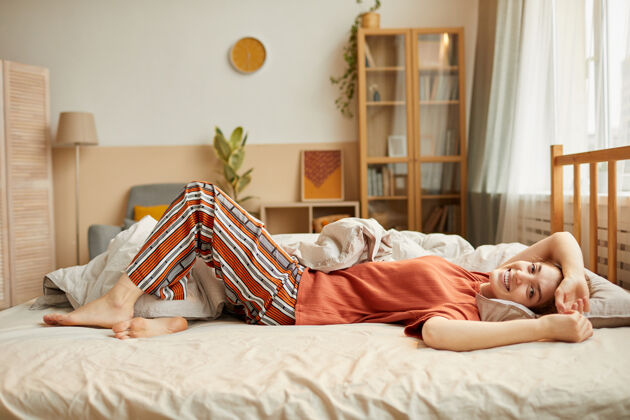 家庭房间身着家装的年轻女子在床上放松 在家享受周末的写真躺下公寓微笑