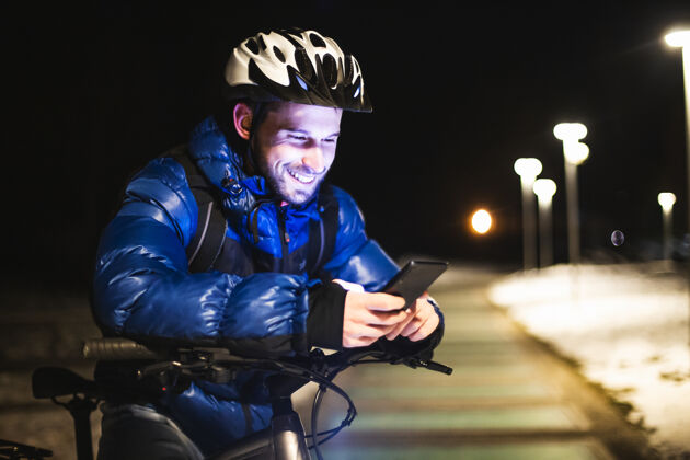 健康晚上 在城外的一个公园里 一个年轻的快递员骑着自行车 用智能手机和gps检查顾客的地址头盔人户外