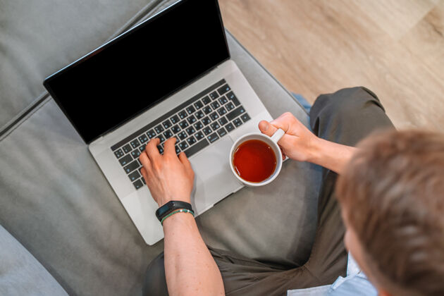 网络研讨会一名男子坐在沙发上远程工作时使用笔记本电脑原点距离在线教育坐互联网学习