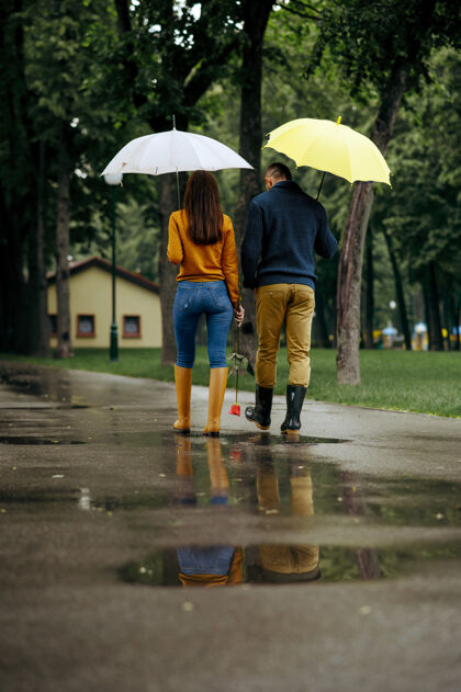 季节带着雨伞的情侣漫步在夏日公园 背景 雨天戴曼女人在雨中的小路上悠闲地走着 小巷里的天气潮湿保护家庭人类
