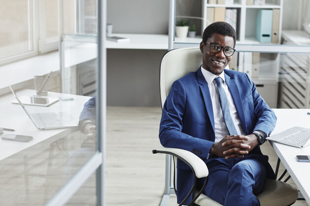 现代非洲成功商人坐在办公室椅子上微笑的画像技术正式服装衣着讲究