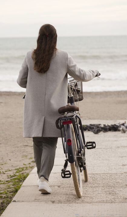 自然黑发女人冬天骑着自行车沿着海边的海滩散步户外男性公园