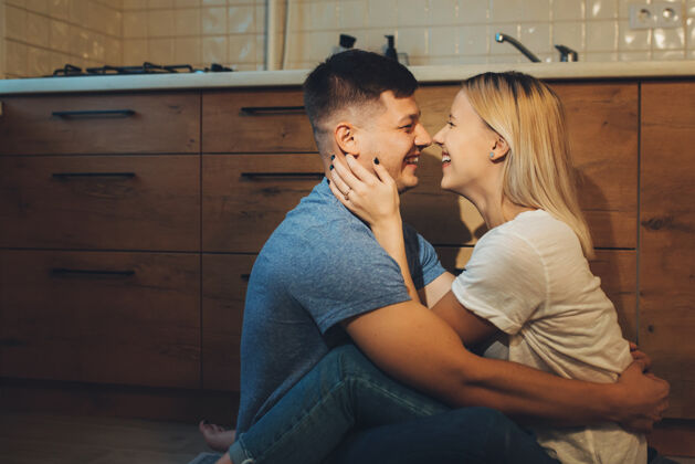 成人一对可爱的年轻夫妇在下班后在厨房的地板上拥抱时大笑的侧视图年轻拥抱娱乐
