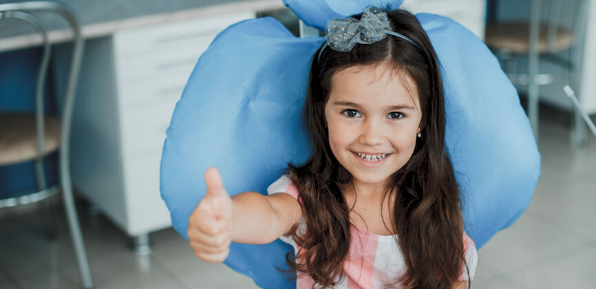 牙痛可爱的小女孩坐在口腔科的椅子上 在牙齿手术后笑着竖起大拇指口腔椅子孩子