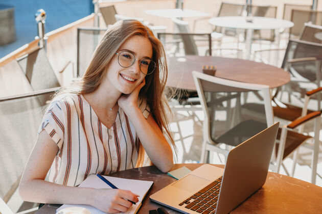 微笑一位红发雀斑的迷人女性在咖啡店的笔记本电脑旁工作时微笑的画像商业女性会议积极