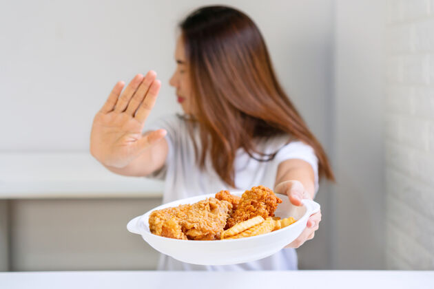 卡路里年轻女子的手推开她最喜欢的油炸食品鸡肉健康食物概念.deny不健康的饮食观念膳食人人