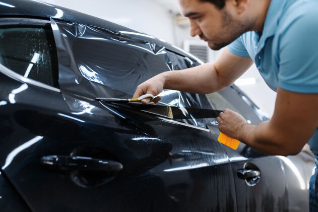 工人男工人拿着胶卷 汽车调色装置 调音维修机械师在车库的车窗上涂乙烯基色 有色汽车玻璃汽车工艺工具