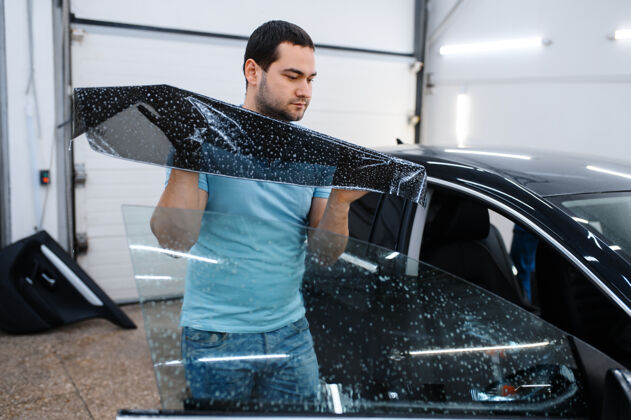 专家男性专业安装湿车染色 调音维修机械师在车库的车窗上涂乙烯基色 有色汽车玻璃设备专业车库