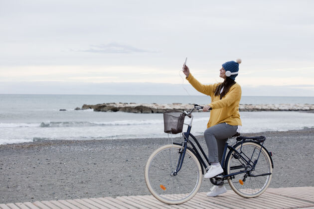 运动优雅的女人骑自行车和使用手机电话.by大海 黄色的毛衣和耳机空间为文本活动自行车海洋