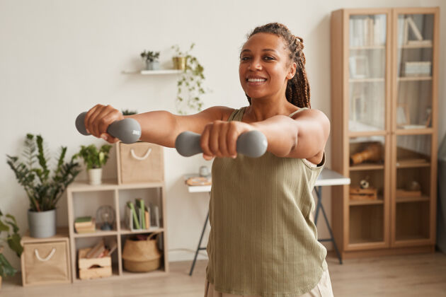 信心年轻的微笑的女人站在家里的房间里练习哑铃健康运动锻炼设备