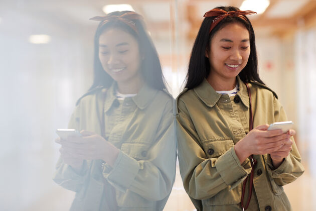 东亚民族穿着休闲服的亚洲年轻女子一边微笑着一边用手机打字电话亚洲和印度民族自信