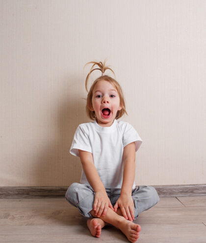 童年一个漂亮的小女孩坐在家里靠墙的地板上做鬼脸一个有趣的童年房间笑脸孩子