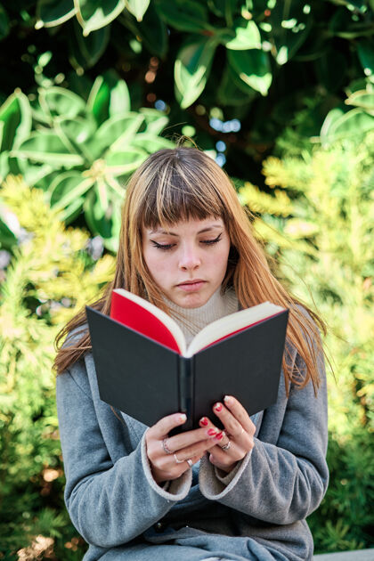 成人一张蓝眼睛的白人金发年轻女子在公园看书的特写照教育金发年轻