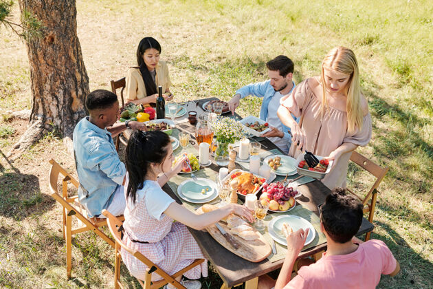 男孩穿着休闲装的年轻金发女性在和朋友共进晚餐时站在餐桌旁 从碗里拿出一些煮熟的蔬菜午餐女儿健康饮食