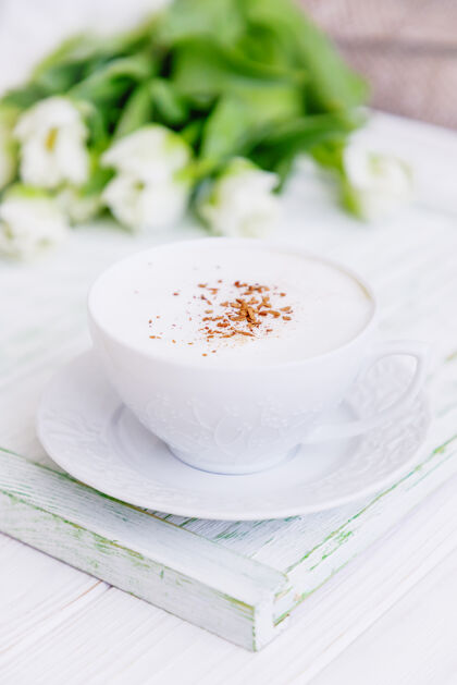 白杯子咖啡卡布奇诺与锡兰肉桂在一个白色的杯子和白色郁金香花木头饮料