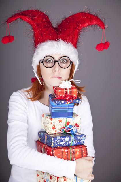 无忧无虑滑稽的红发女孩戴着圣诞帽 手里拿着礼品盒举行长享受