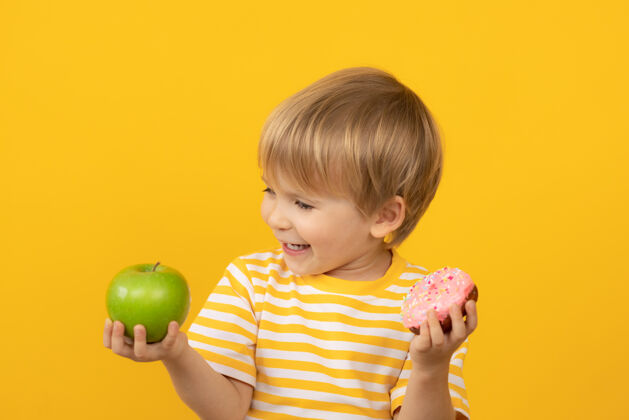 不健康快乐的孩子拿着甜甜圈和苹果素食小吃搞笑
