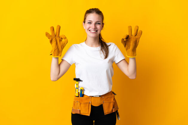 人一位年轻的电工女士被隔离在黄色区域 用手指显示“ok”标志工具女人木工