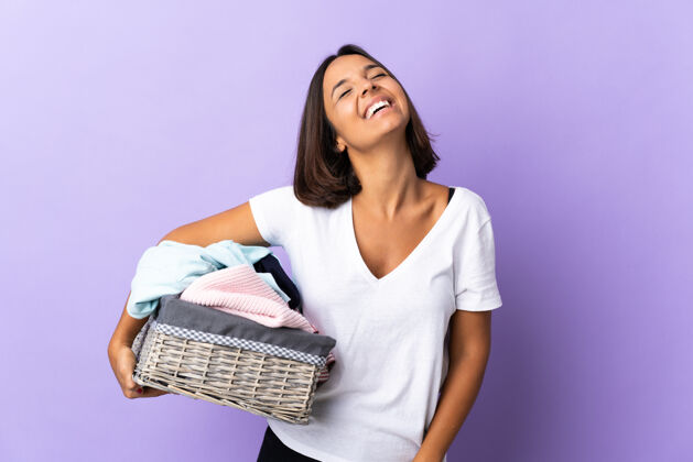 自信年轻的拉丁女子拿着一个衣篮孤立地笑着对紫色洗人湿