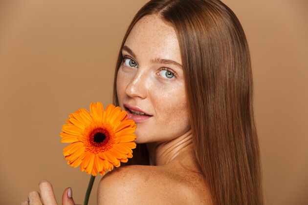 自然美丽的肖像画一个美丽健康的年轻女子长着红色的头发显示橙色赫伯拉花隔离在米色墙上女人脸女性