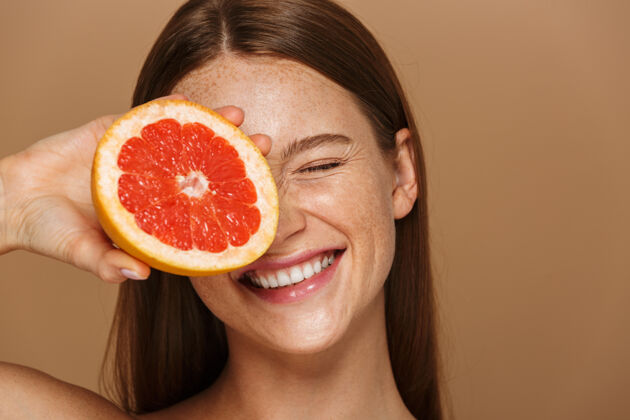 饮食美丽的肖像 一个美丽健康的年轻裸体女子长着红色的头发显示切片柚子隔离在米色墙上葡萄柚身体微笑